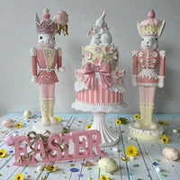 Pink Easter bunny nutcrackers with floral cake, pastel eggs, and 'EASTER' sign for spring home décor