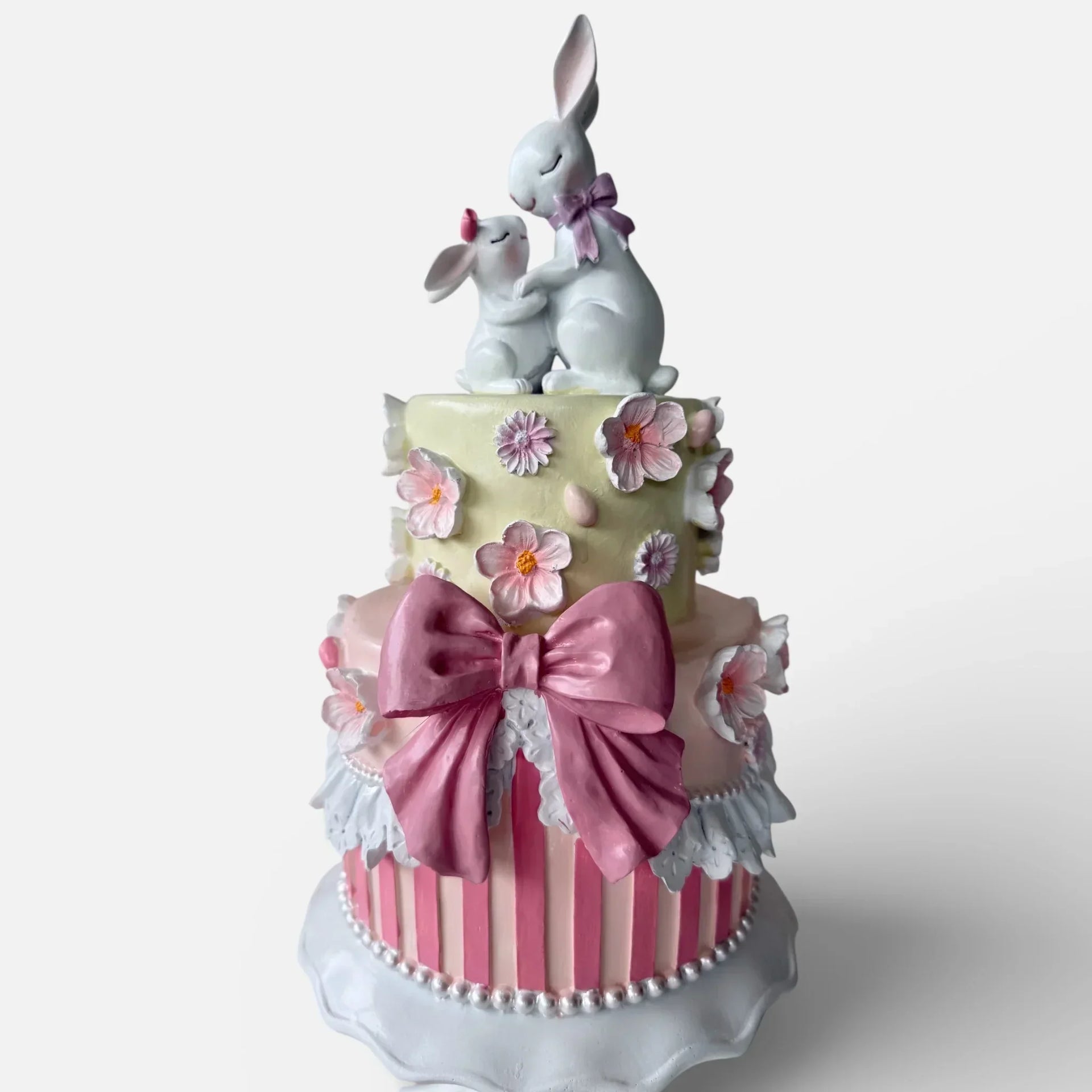 Charming two-tier cake decor with pink bow, floral details, and bunny figurines for home décor