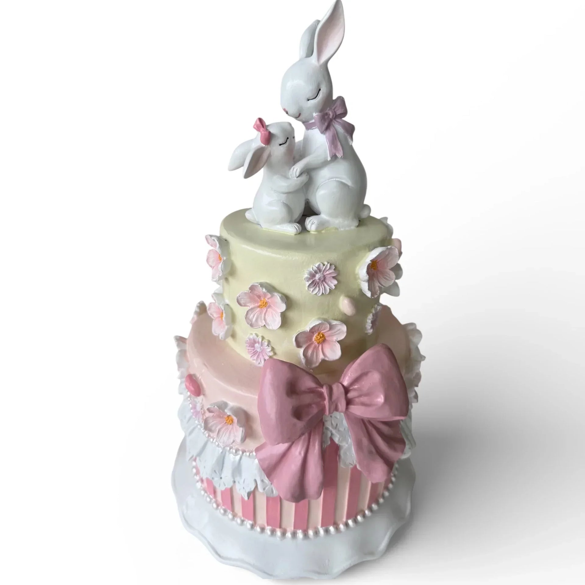 Charming two-tier cake decor with white bunnies, pink bow, and floral accents for home décor