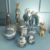 Easter bunny figurines, blue ceramic decor, and vintage-style home accessories on a pastel table