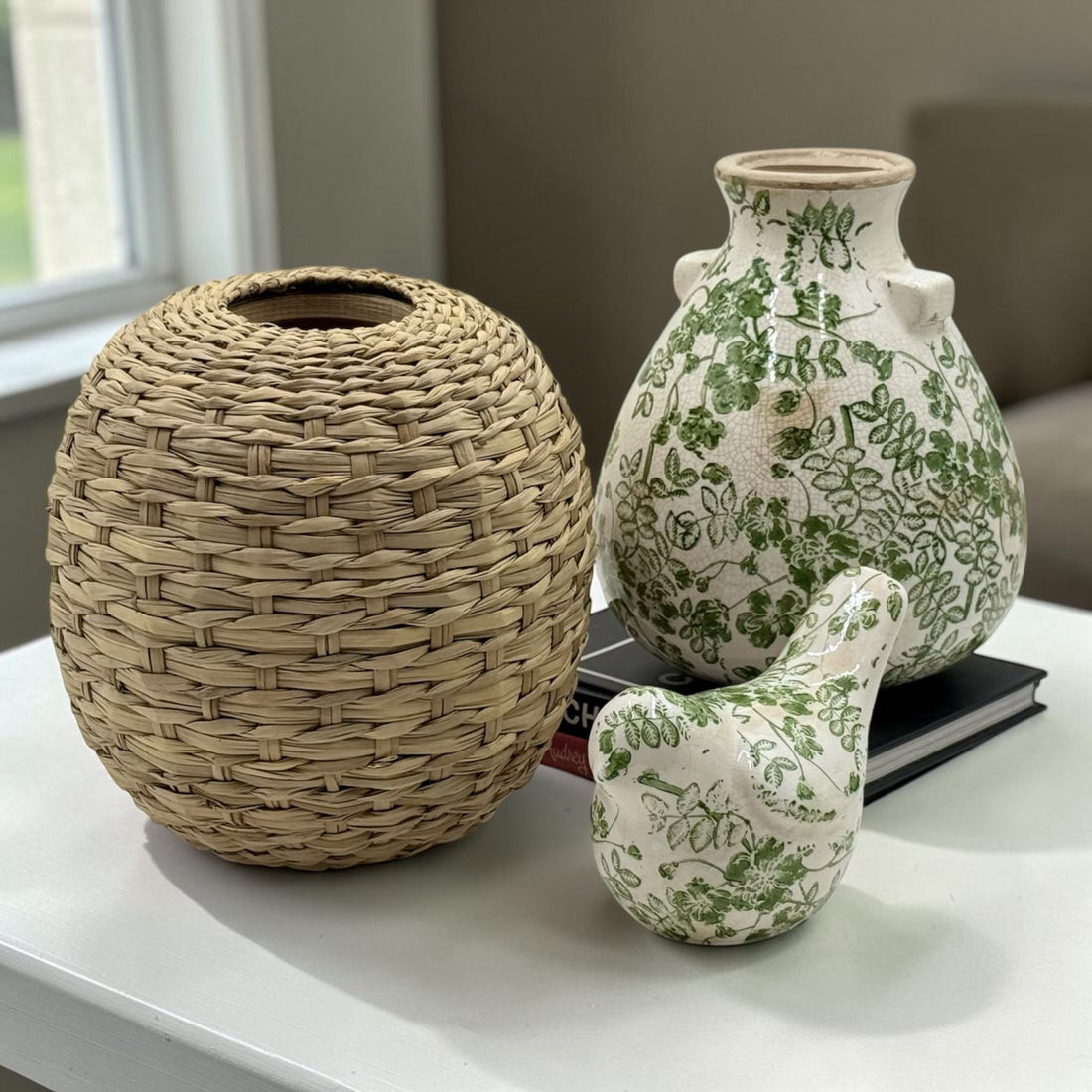 Darlin green floral ceramic vase and bird figurine beside a woven straw basket on a white table