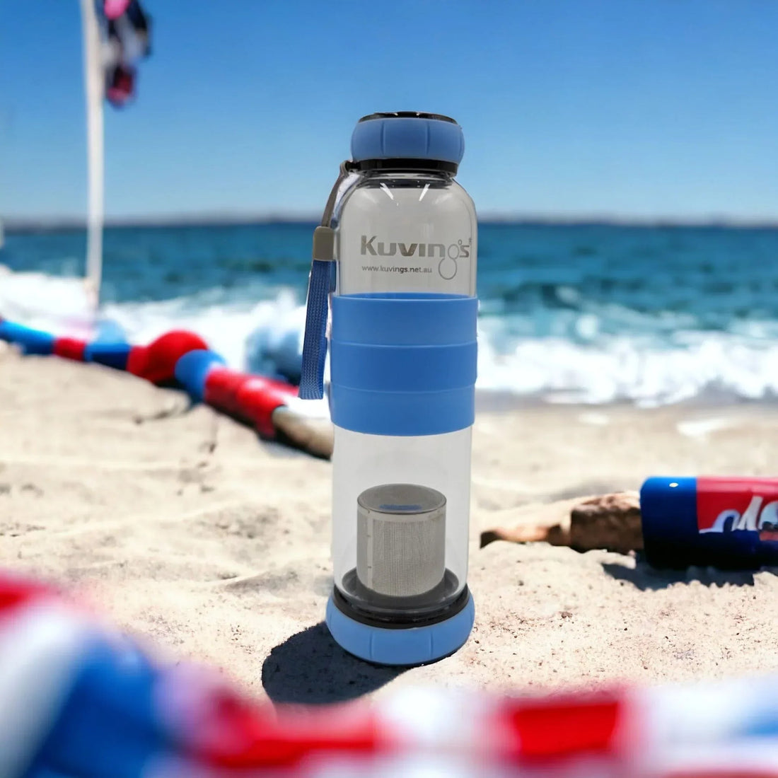 Blue Kuving's water bottle with infuser on sandy beach, ocean waves background, perfect for outdoor hydration