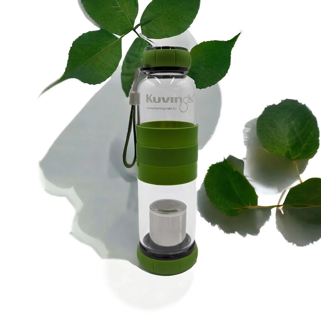 Clear glass tea infuser bottle with green silicone grip and lid, featuring a mesh strainer, styled with fresh green leaves.