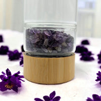 Amethyst crystal chips in glass jar with bamboo base, surrounded by purple flowers for home décor
