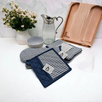 Blue and white striped oven mitts and pot holders with wooden tray, glass pitcher, and floral vase on marble countertop