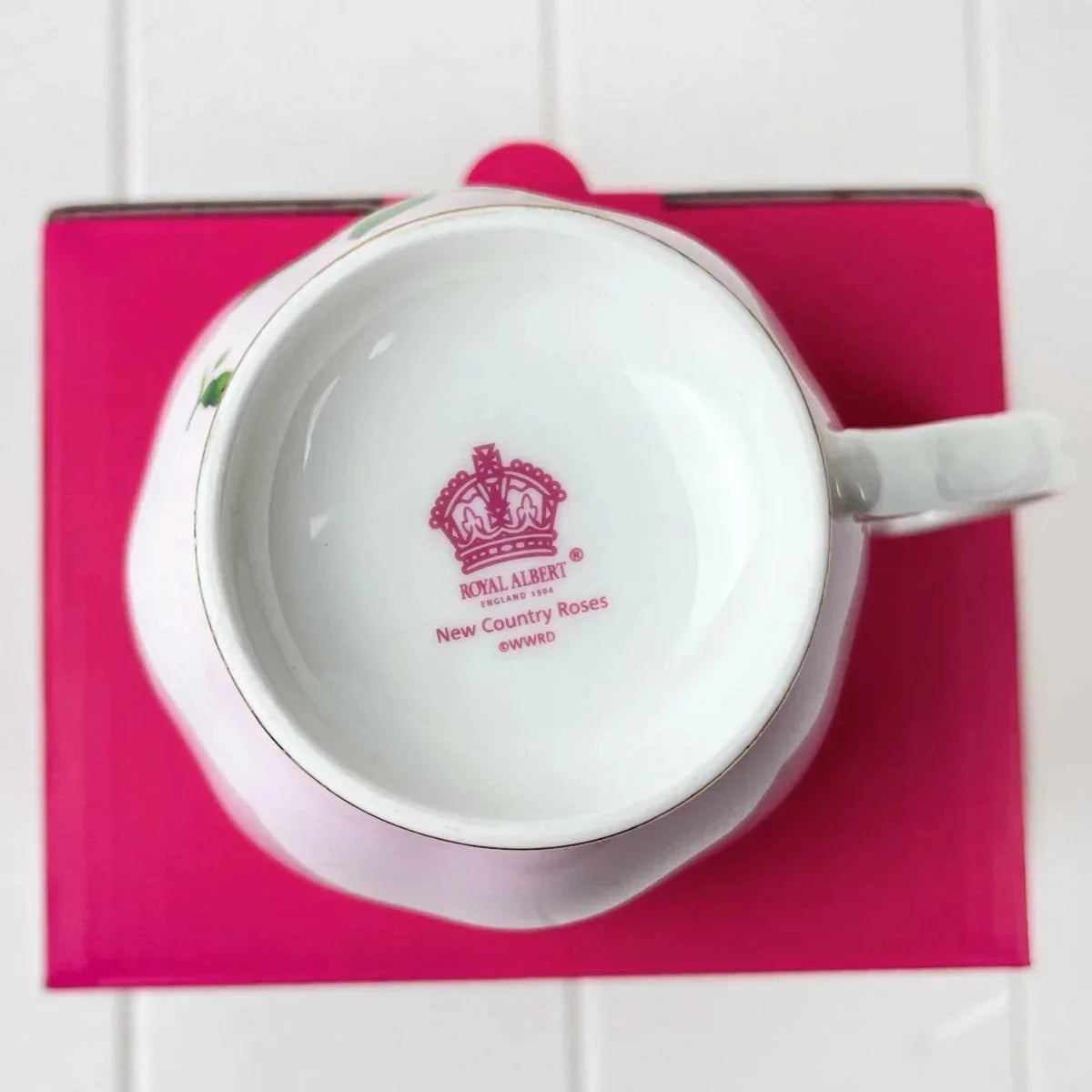 Royal Albert New Country Roses teacup with pink crown logo on white porcelain, set on vibrant pink base